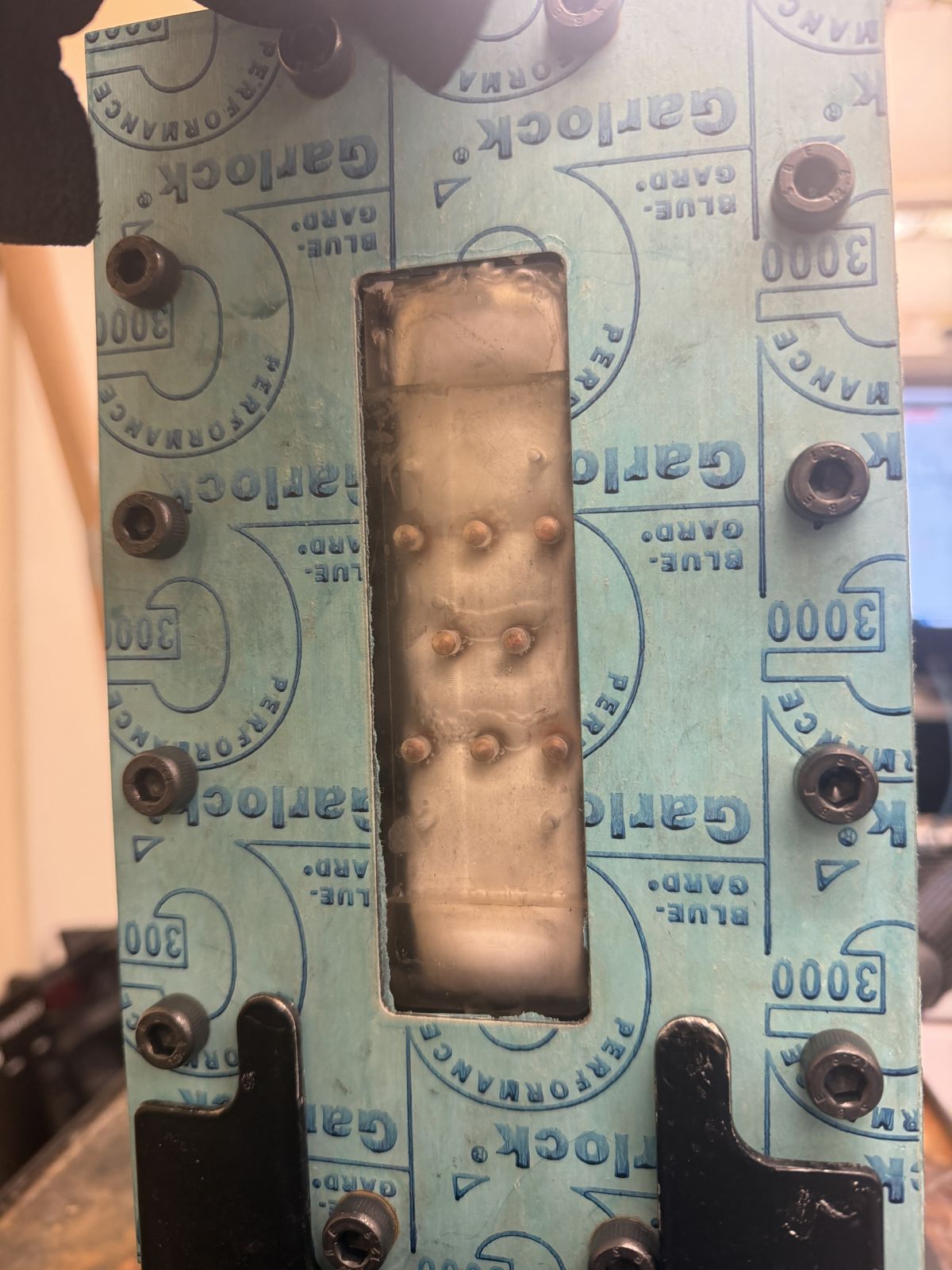Rotated close-up through a Garlock gasket sheet window showing the same finned module insert and pin-fin contacts inside the housing cavity.