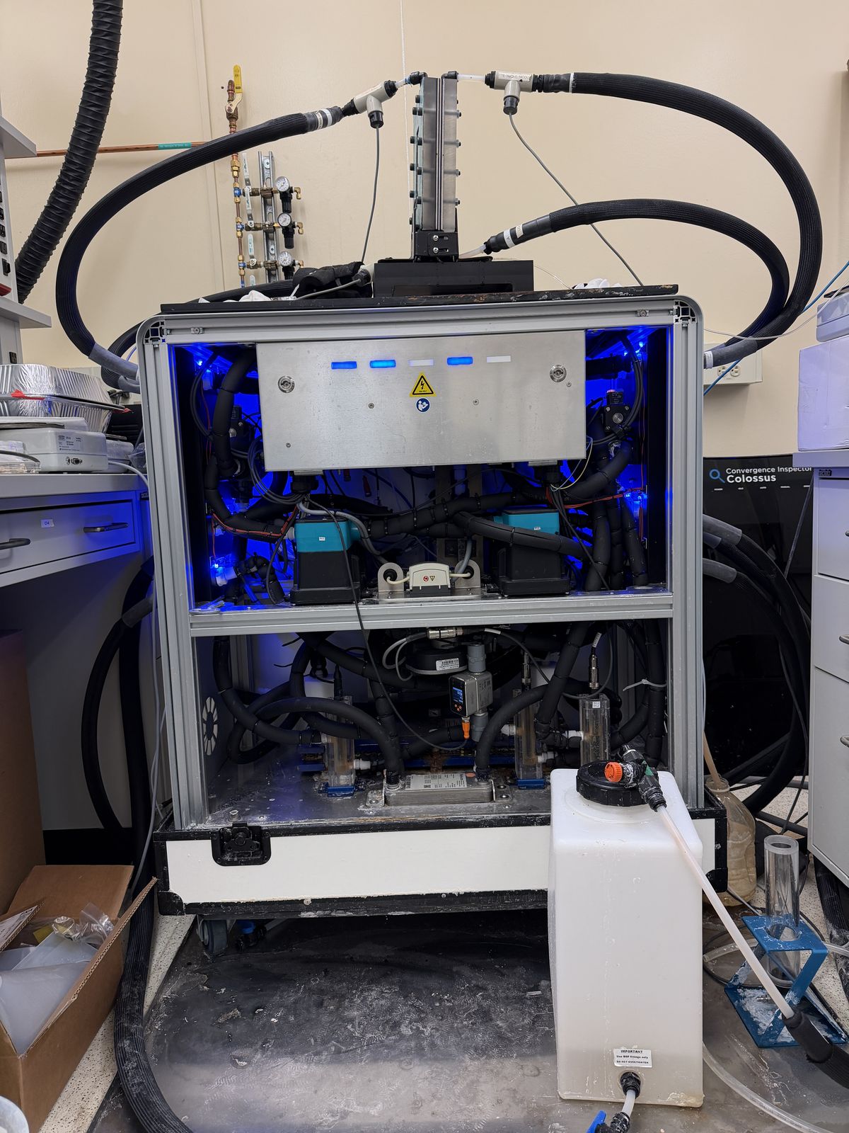 The unlabeled membrane distillation test rig in the Warsinger Lab, showing the aluminum extrusion frame, tubing loops, blue indicator lights, pumps, and feed reservoir.